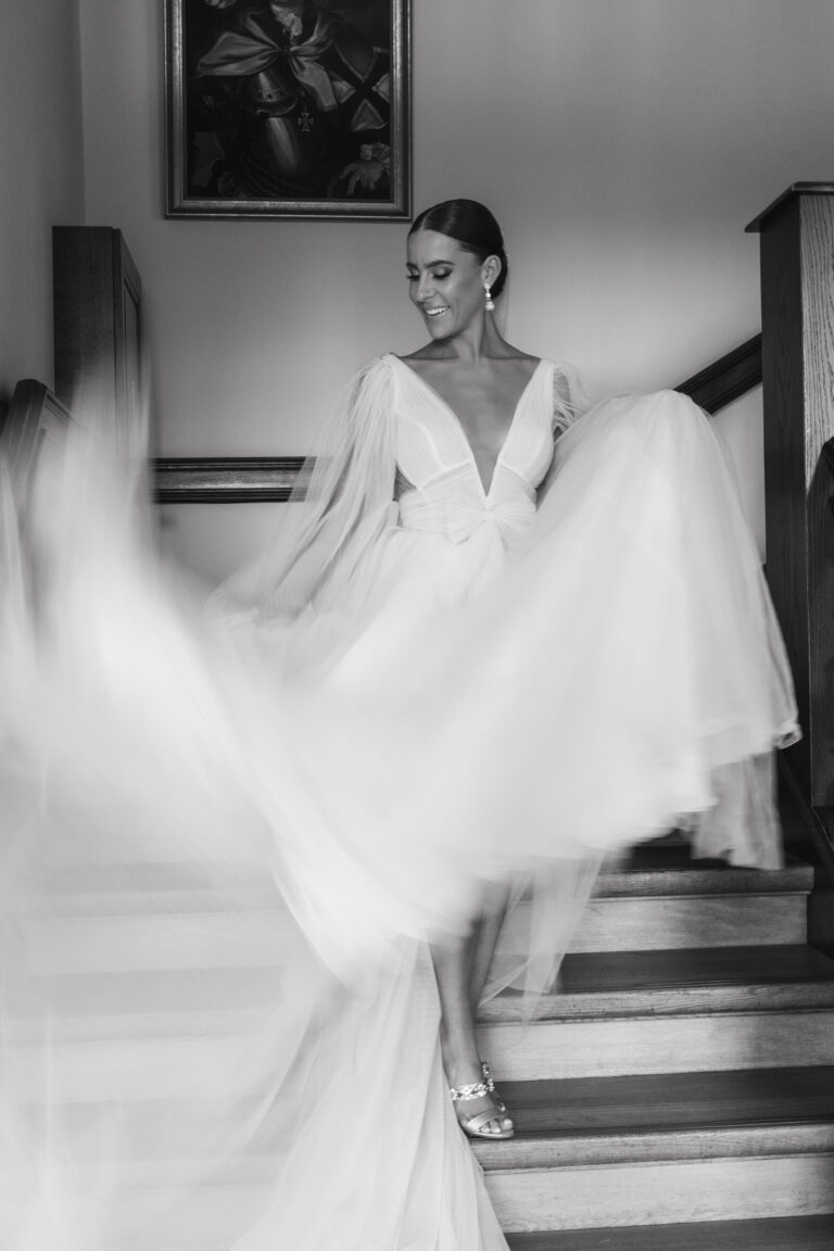 Eine Braut in einem wallenden Kleid wirbelt auf einer Treppe, ihr Kleid wogt, und sie lächelt nach unten.