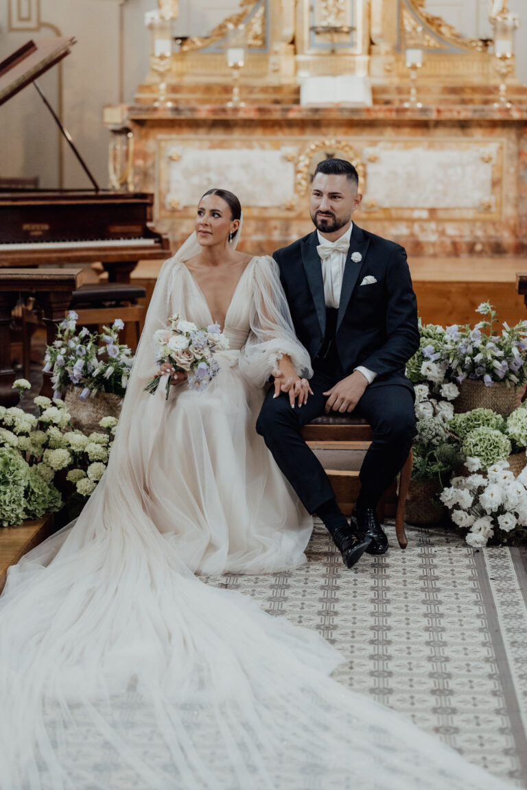 Braut und Bräutigam sitzen zusammen in einer geschmückten Kirche und halten sich während ihrer Hochzeitszeremonie an den Händen.