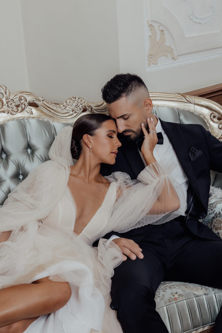 Braut und Bräutigam sitzen auf einem alten Sofa und umarmen sich zärtlich in eleganter Hochzeitskleidung.