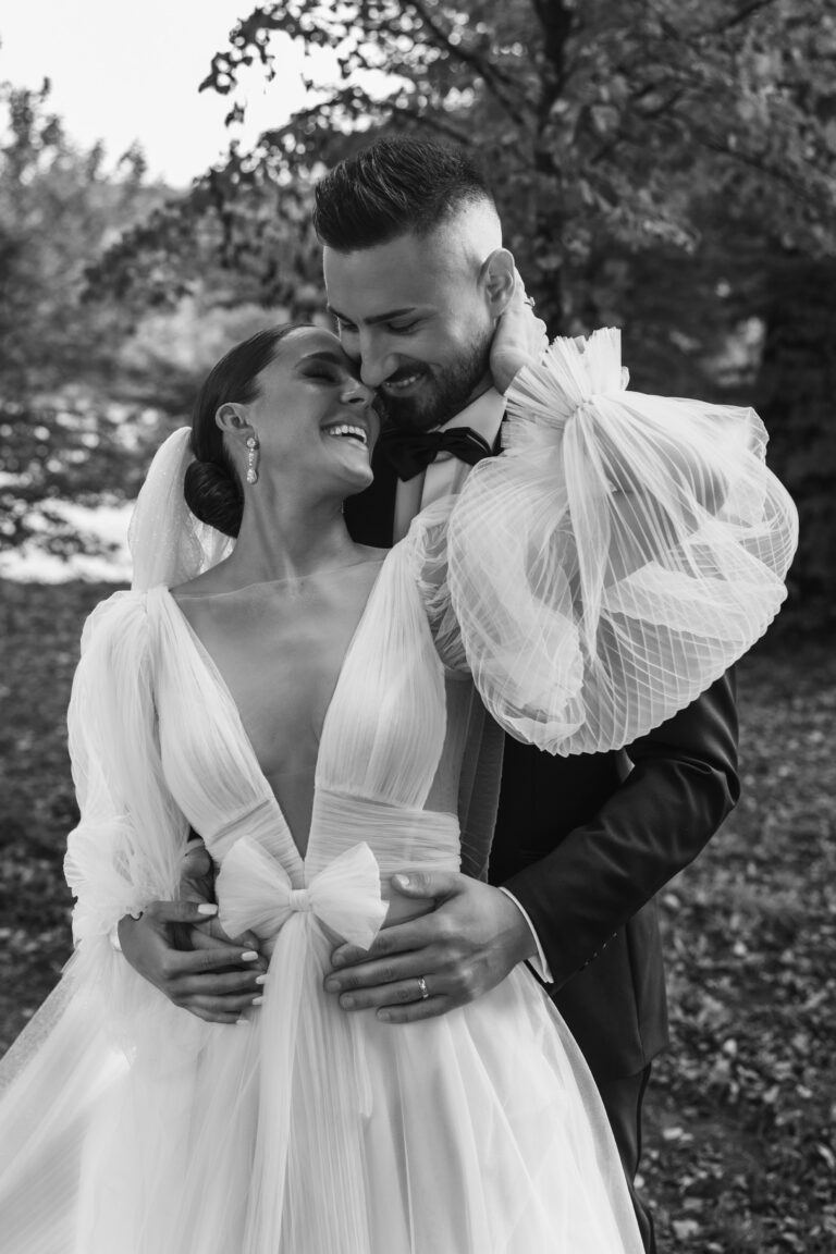 Eine Braut und ein Bräutigam umarmen sich an ihrem Hochzeitstag im Freien und lächeln sich gegenseitig an.