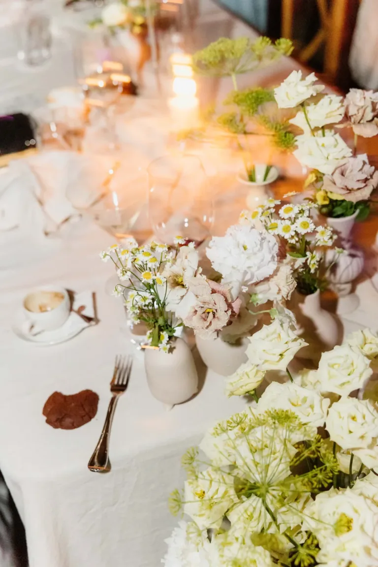 Elegante Tischdekoration mit weißen Blumen, Kerzen, einer Kaffeetasse und einem einzelnen Keks auf einer weißen Tischdecke.
