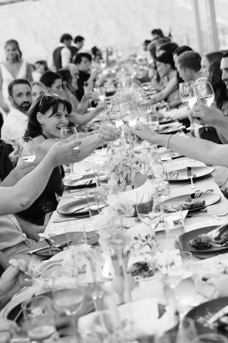 Menschen, die an einem langen Tisch sitzen und bei einer feierlichen Veranstaltung mit einem festlichen Toast die Gläser anstoßen.