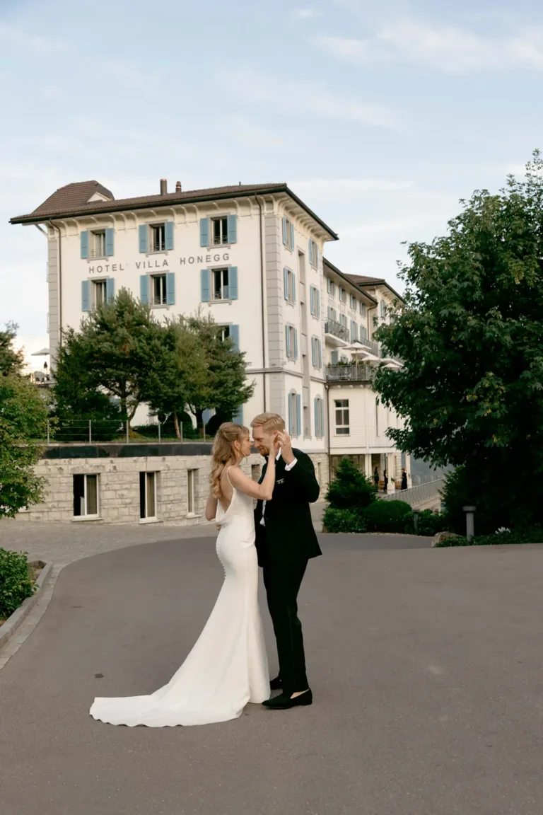 Ein Brautpaar tanzt vor dem Hotel Villa Honegg, umgeben von Bäumen und eleganter Architektur.