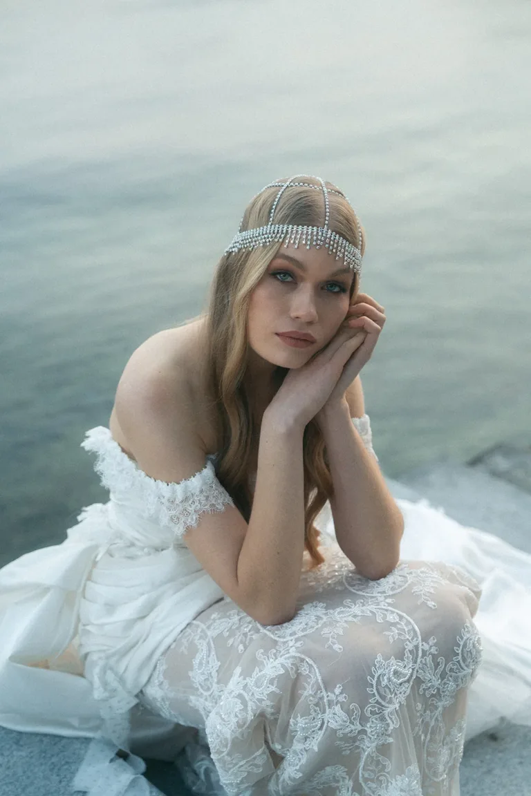 Eine Frau in einem weißen Spitzenhochzeitskleid mit einem mit Edelsteinen besetzten Kopfschmuck bei einer luxuriösen Hochzeit in der Schweiz.