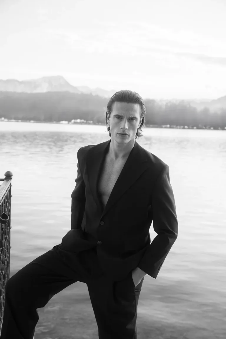 Ein Mann in einem dunklen Sakko, das er ohne Hemd trägt, steht an einem See anlässlich einer luxuriösen Hochzeit, Luxury Wedding Planner, Zurich, The WES, Switzerland, Schweiz, Lara Flueckiger, Grand Hotel National, Luzern