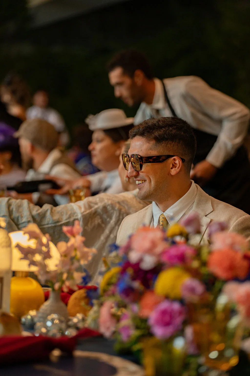 Ein Mann in einem weißen Anzug und mit Sonnenbrille lächelt am Esstisch – perfekt für Corporate Events Schweiz.