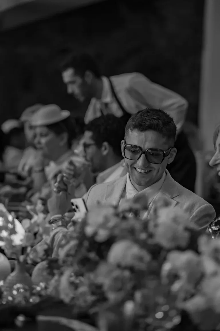 Ein Mann mit Brille und im Anzug lächelt während der Corporate Events Schweiz in Richtung eines mit Blumen geschmückten Esstisches. Corporate Event Schweiz, Firmenevent planen, Private Events