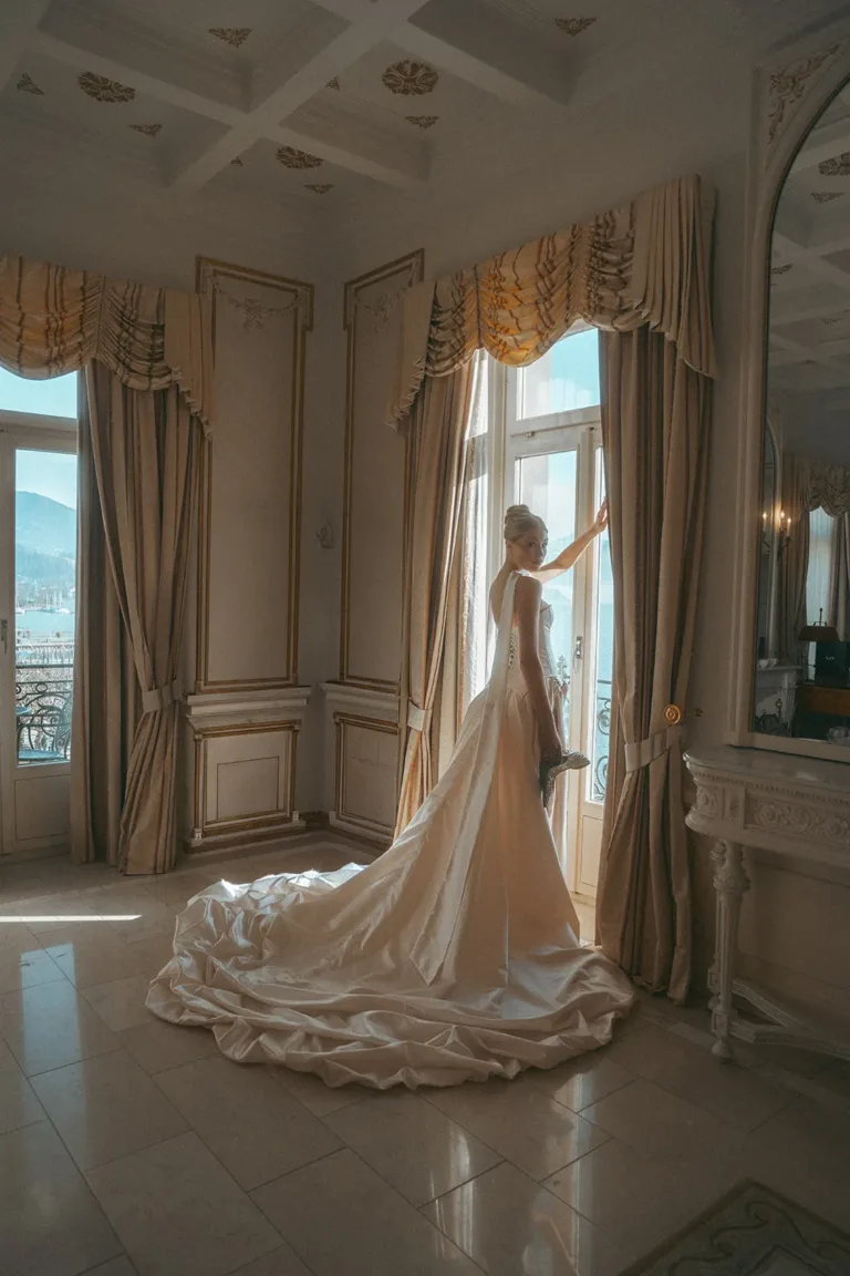 Eine Braut in einem langen Kleid vor einem Fenster, fotografiert von einem Luxus-Hochzeitsplaner in der Schweiz, Luxury Wedding Planner, Zurich, The WES, Switzerland, Schweiz, Lara Flueckiger, Grand Hotel National, Luzern