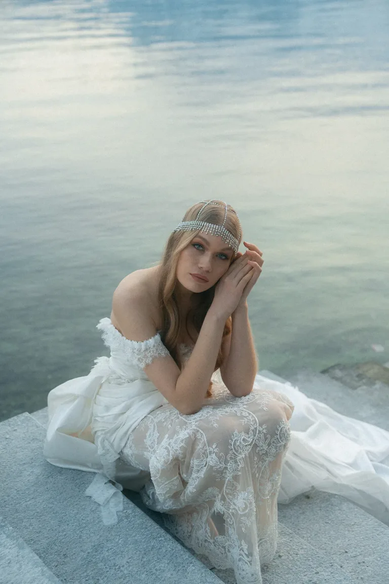 Eine Braut in einem Spitzenhochzeitskleid und mit einem Kristall-Kopfschmuck auf den Steinstufen einer Schweizer Hochzeitslocation,Luxury Wedding Planner, Zurich, The WES, Switzerland, Schweiz, Lara Flueckiger, Grand Hotel National, Luzern
