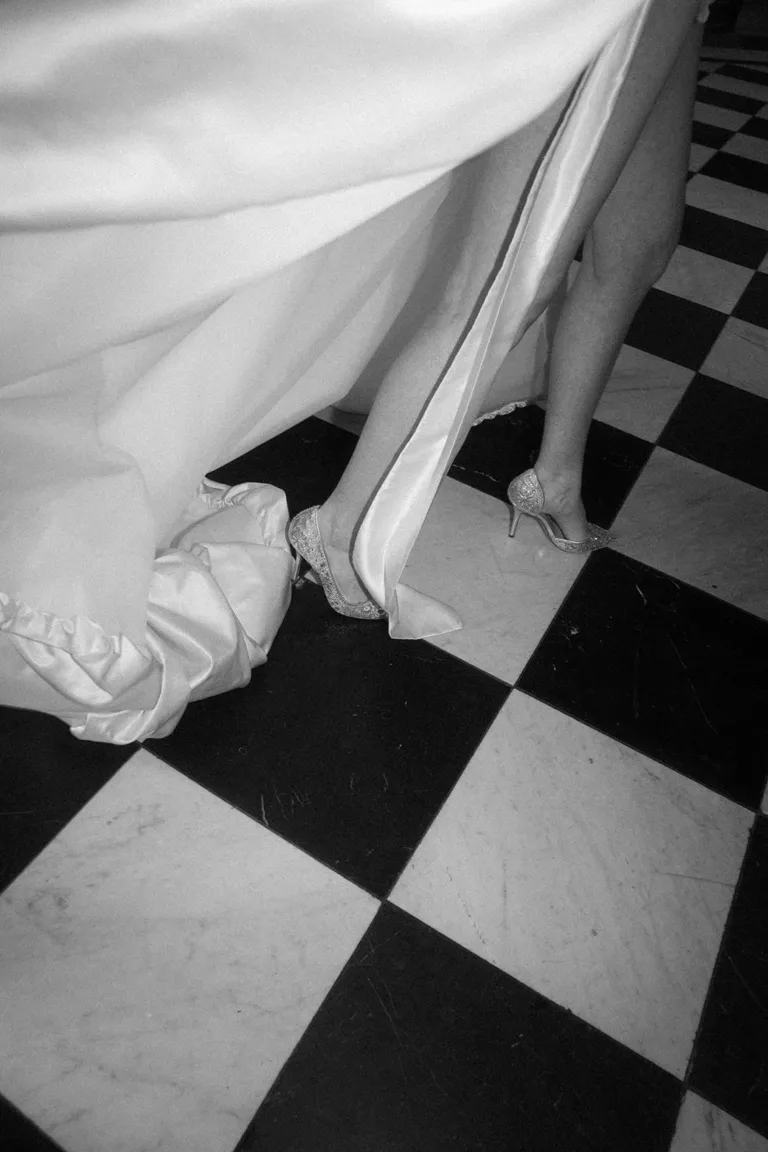 Eine Person in einem weißen Kleid und verzierten Pumps, die bei einer luxuriösen Hochzeit über einen karierten Boden geht, Luxury Wedding Planner, Zurich, The WES, Switzerland, Schweiz, Lara Flueckiger, Grand Hotel National, Luzern