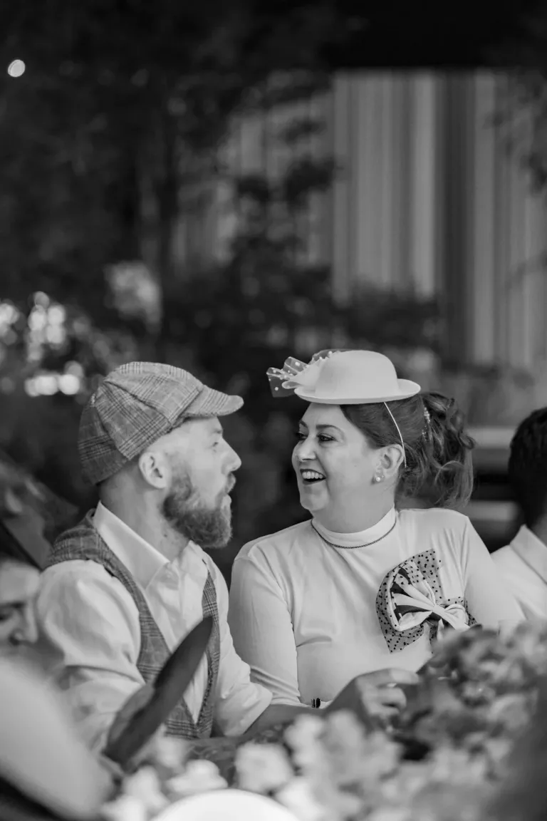 Ein Mann und eine Frau in Retro-Outfits lächeln bei Corporate Events Schweiz im Freien auf einen festlich gedeckten Tisch.